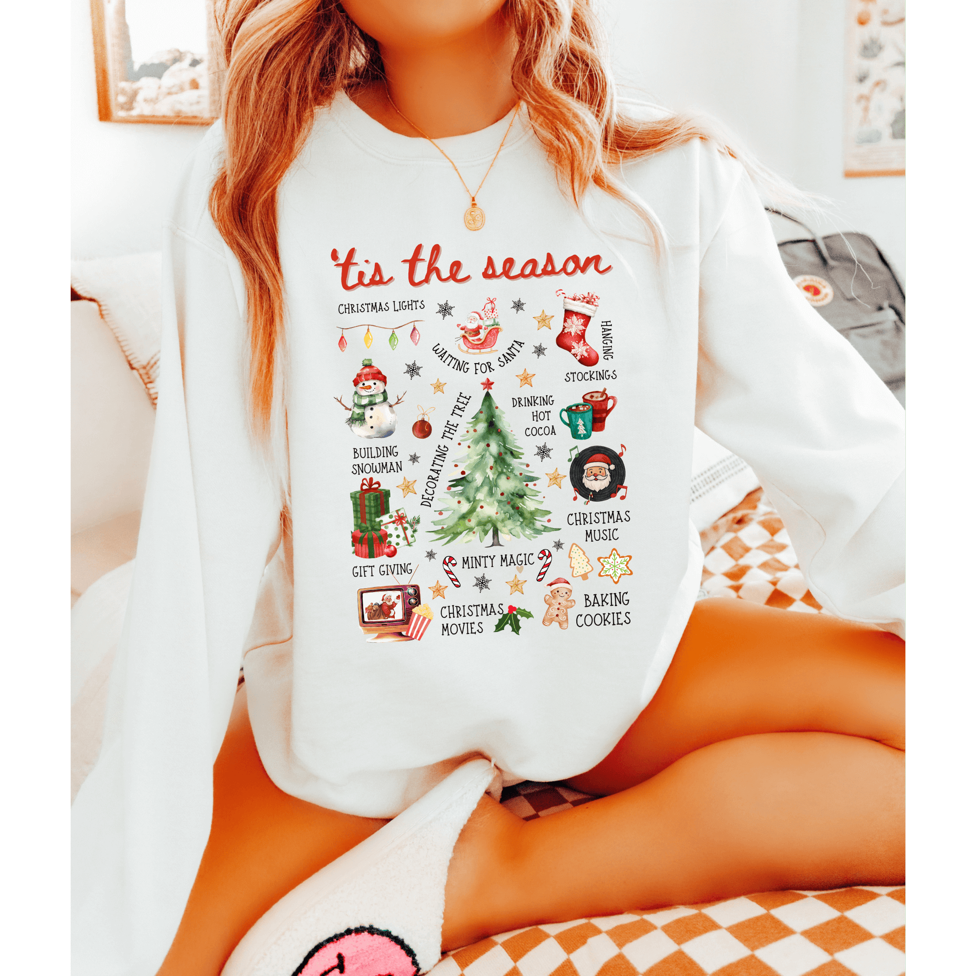 Person wearing a white sweatshirt with Christmas-themed graphics and text.