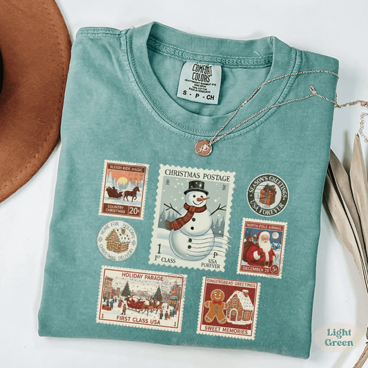 Christmas Postage Stamp Shirt Comfort Colors in light green with vintage holiday stamp designs of snowman, Santa, gingerbread, and Christmas parade