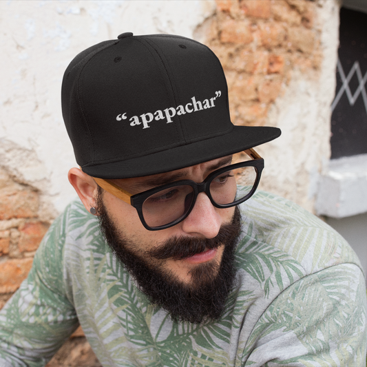 Man wearing a black embroidered snapback hat with the word "apapachar" stitched in white, part of the Manuel Quintero Collection from Zazations.

